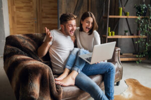 Sonriente joven pareja sentada en el sofá en casa en ropa casual