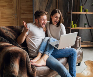 Sonriente joven pareja sentada en el sofá en casa en ropa casual